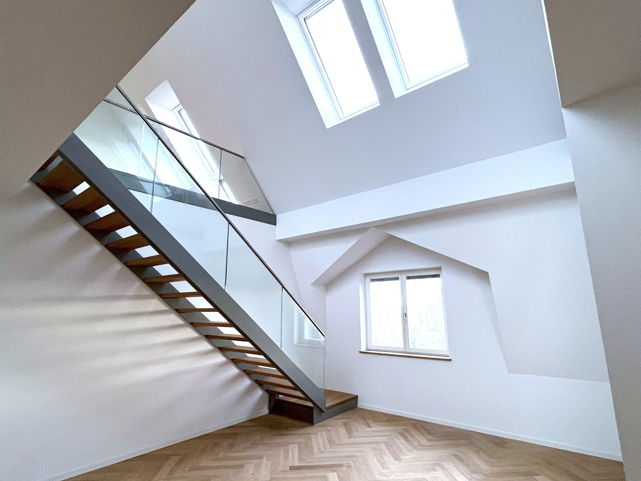 Heller Innenausbau mit offener Treppe, Glasgeländer und Fischgrätparkett