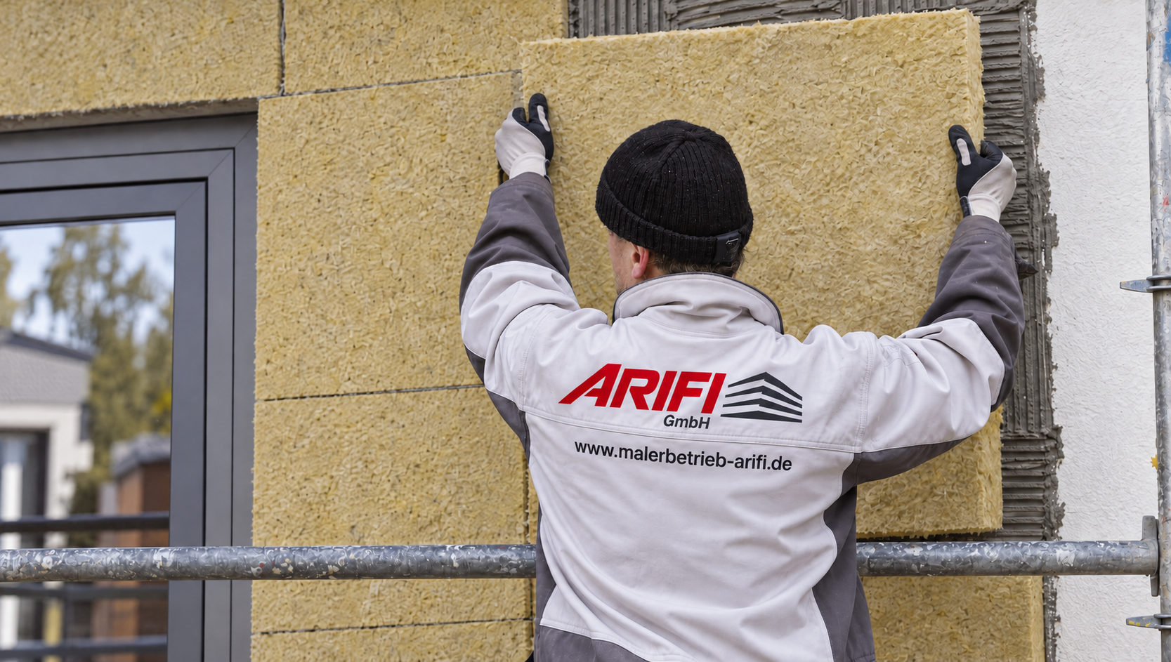 Symbolbild: Mitarbeiter in Arifi-Arbeitskleidung beim Anbringen von Mineralwolldämmung an einer Fassade